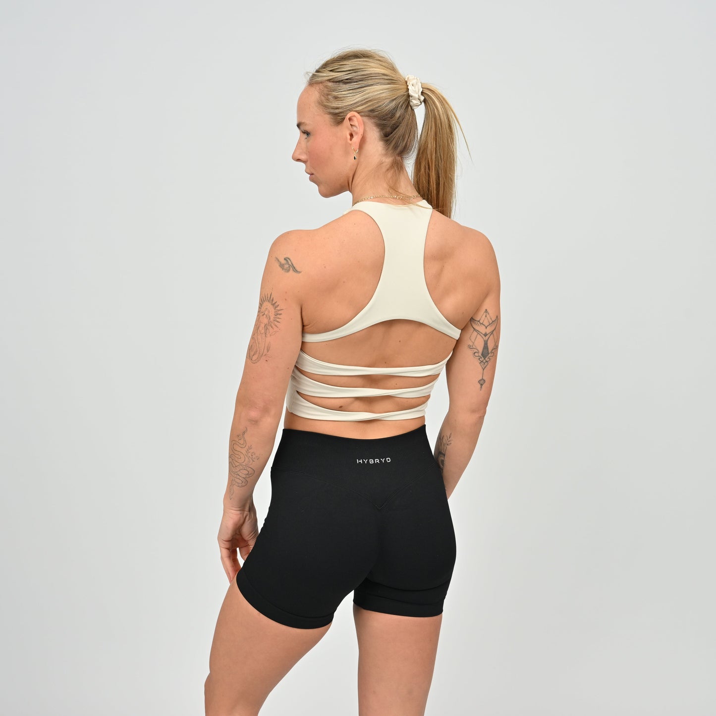 Woman wearing a beige sports bra and black shorts with 'HYBRYD' branding on 
