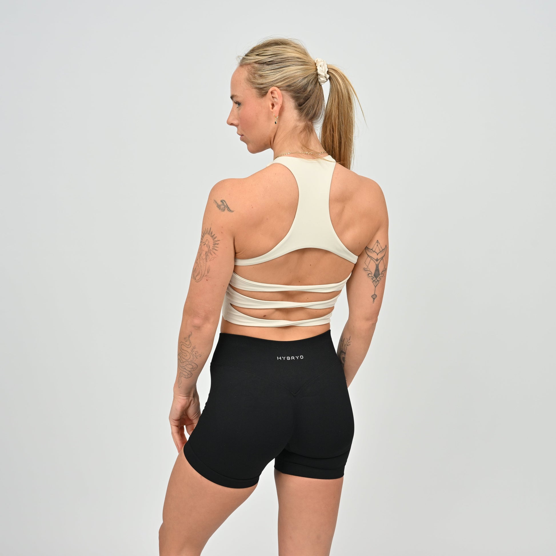 Woman wearing a beige sports bra and black shorts with 'HYBRYD' branding on 