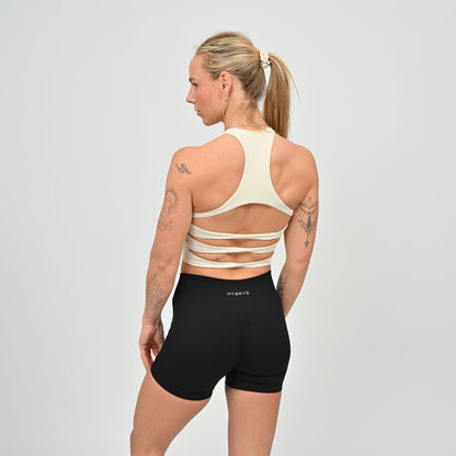 Woman wearing a beige sports bra and black shorts with 'HYBRYD' branding on 