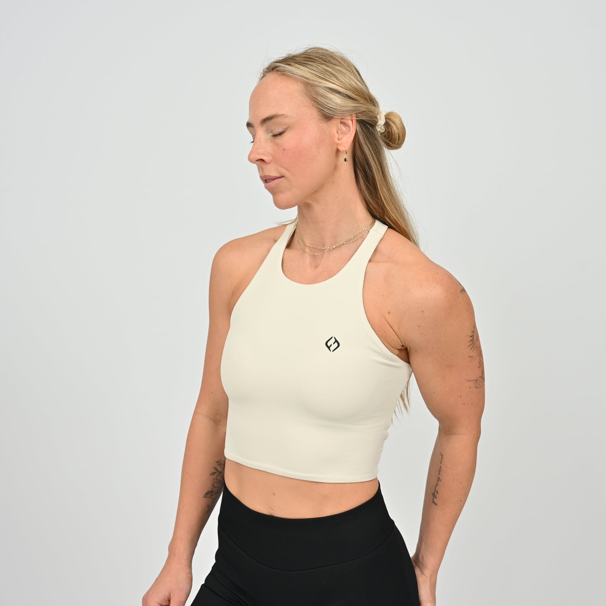 Woman wearing a stone Hybryd sports bra with a small logo from the gymwear brand Hybryd