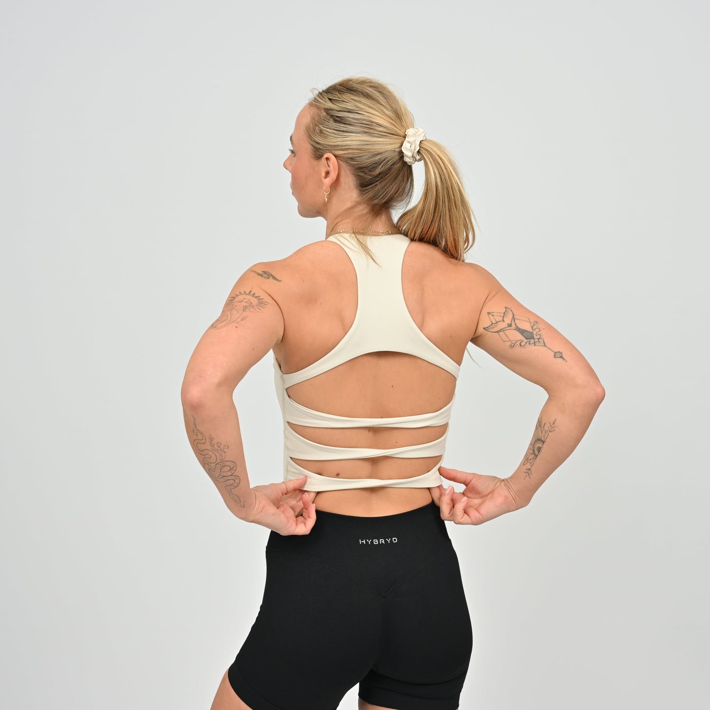 Woman wearing a beige sports bra and black shorts on a gray background