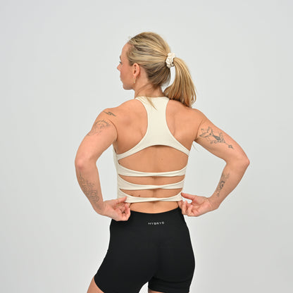 Woman wearing a beige sports bra and black shorts on a gray background