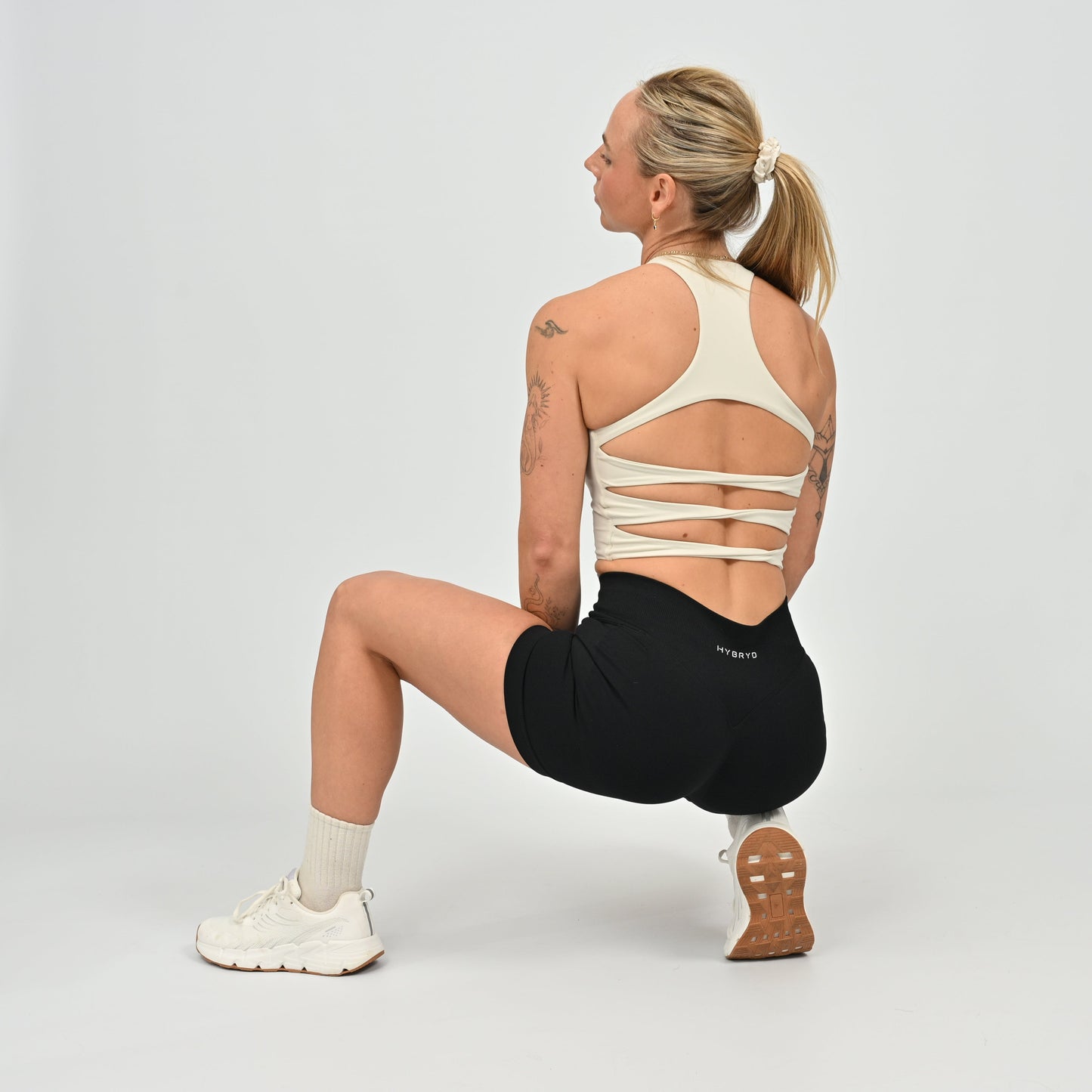 Woman performing a lunge exercise wearing a stone sports bra and black shorts from Hybryd activewear
