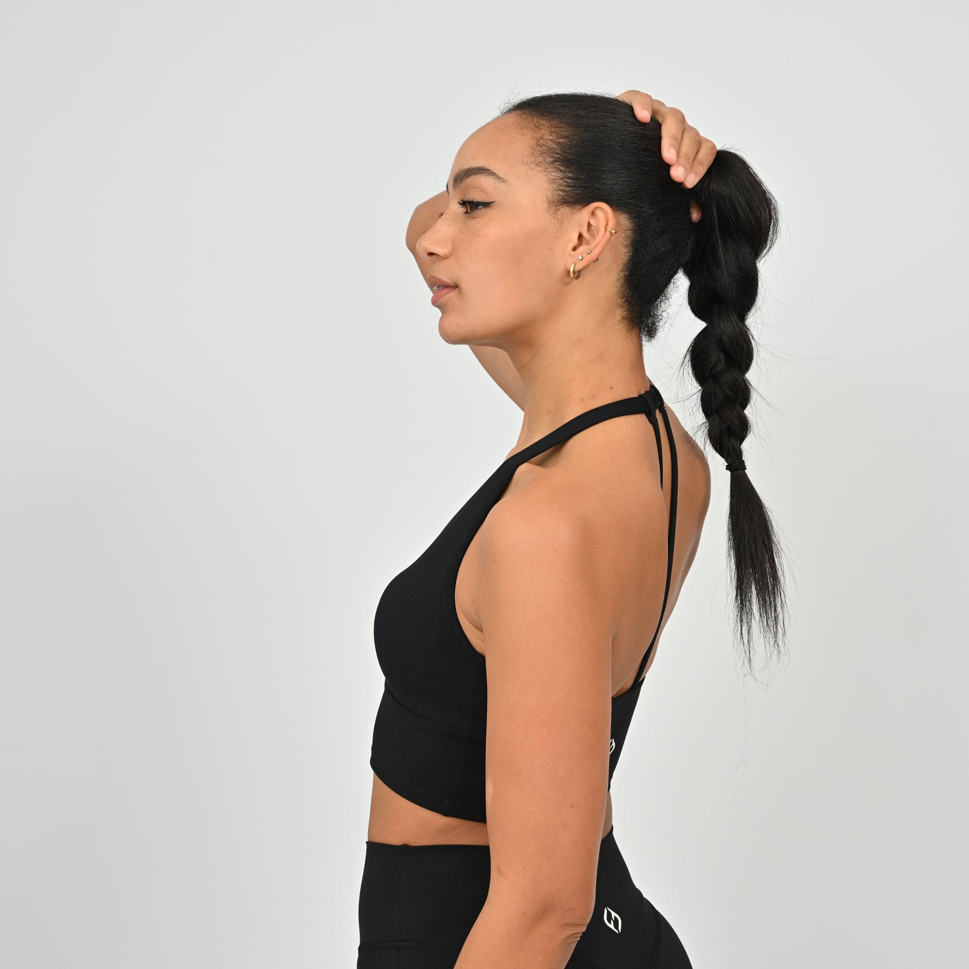 Woman in a black Hybryd sports bra and leggings with her hair in a ponytail against a white background