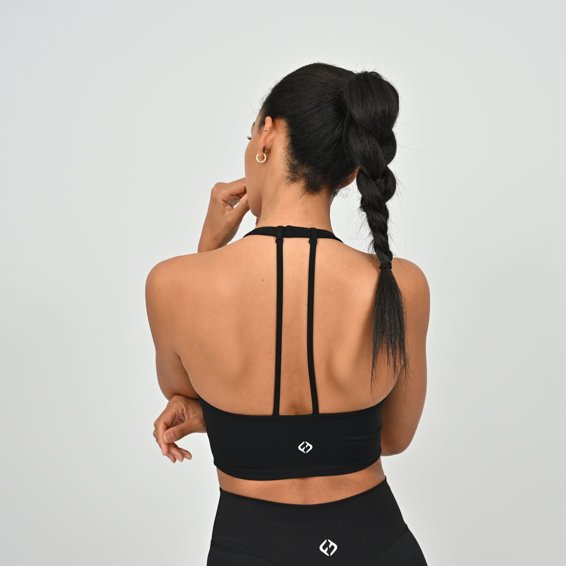 Woman wearing a black Hybryd halter neck sports bra with thin straps on a light gray background