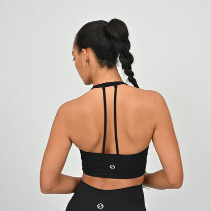 Woman wearing a black Hybryd sports bra with thin straps on a light gray background