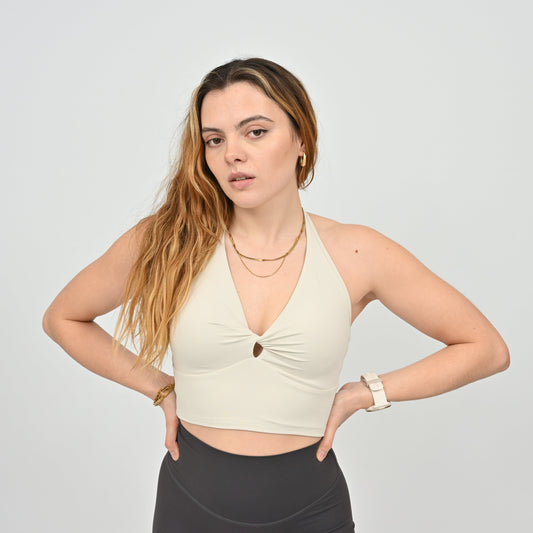 Woman wearing a Hybryd beige halter bra top and black pants on a plain background