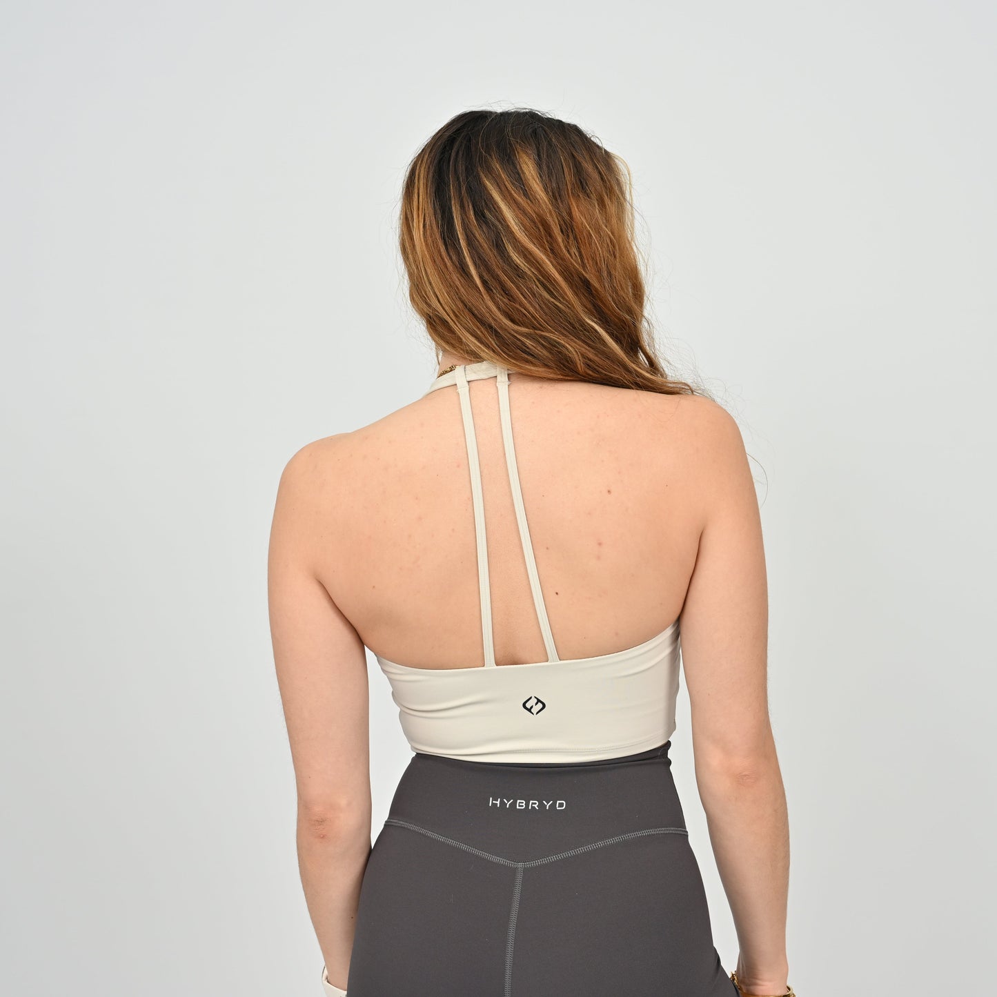 Woman wearing a beige sports bra and gray leggings with 'HYBRYD' branding on a light gray background