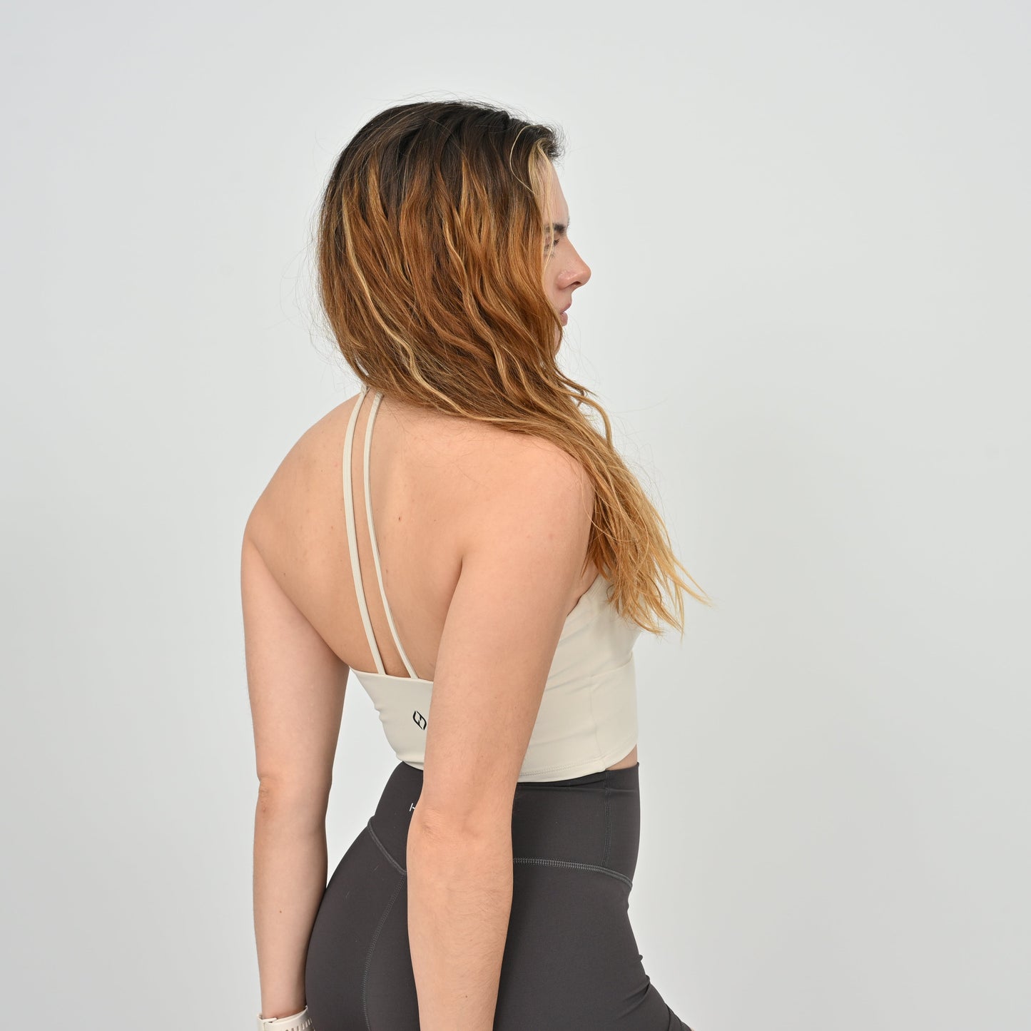 Woman wearing a Hybryd white halter sports bra and gray leggings on a plain background