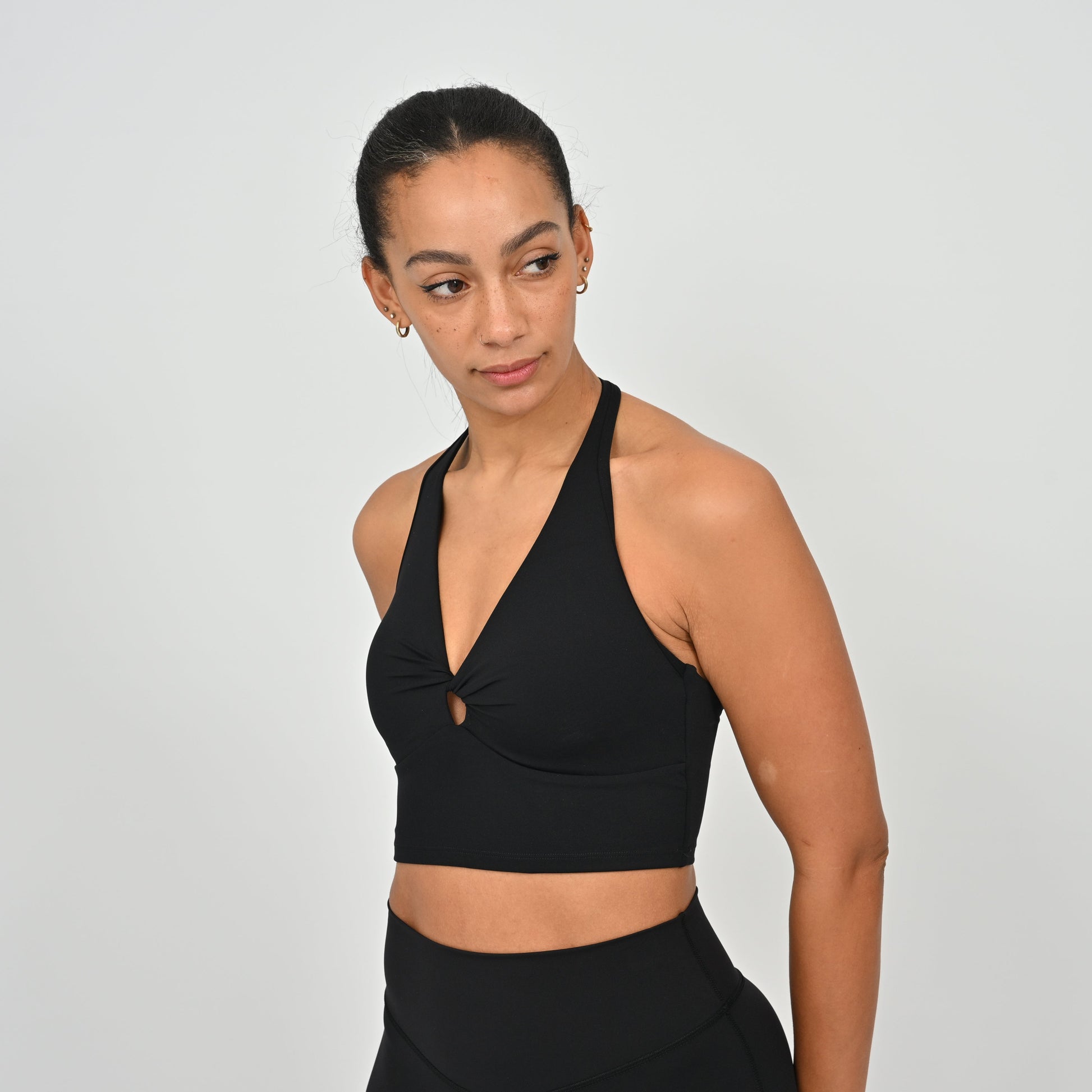 Woman wearing a black Hybryd sports bra and leggings on a light gray background