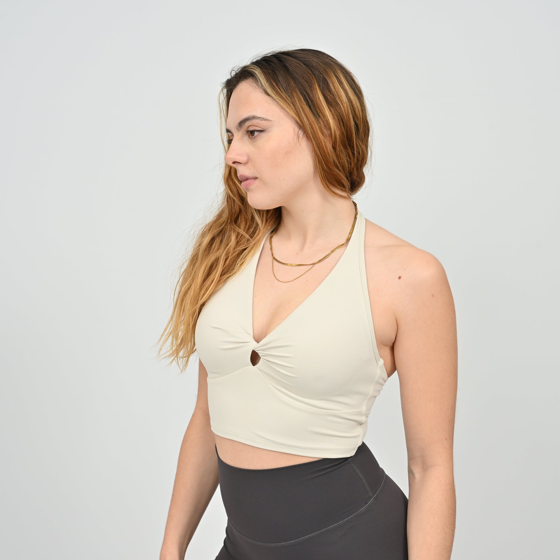 Woman wearing a stone sports bra and Hybryd dark pants on a plain background