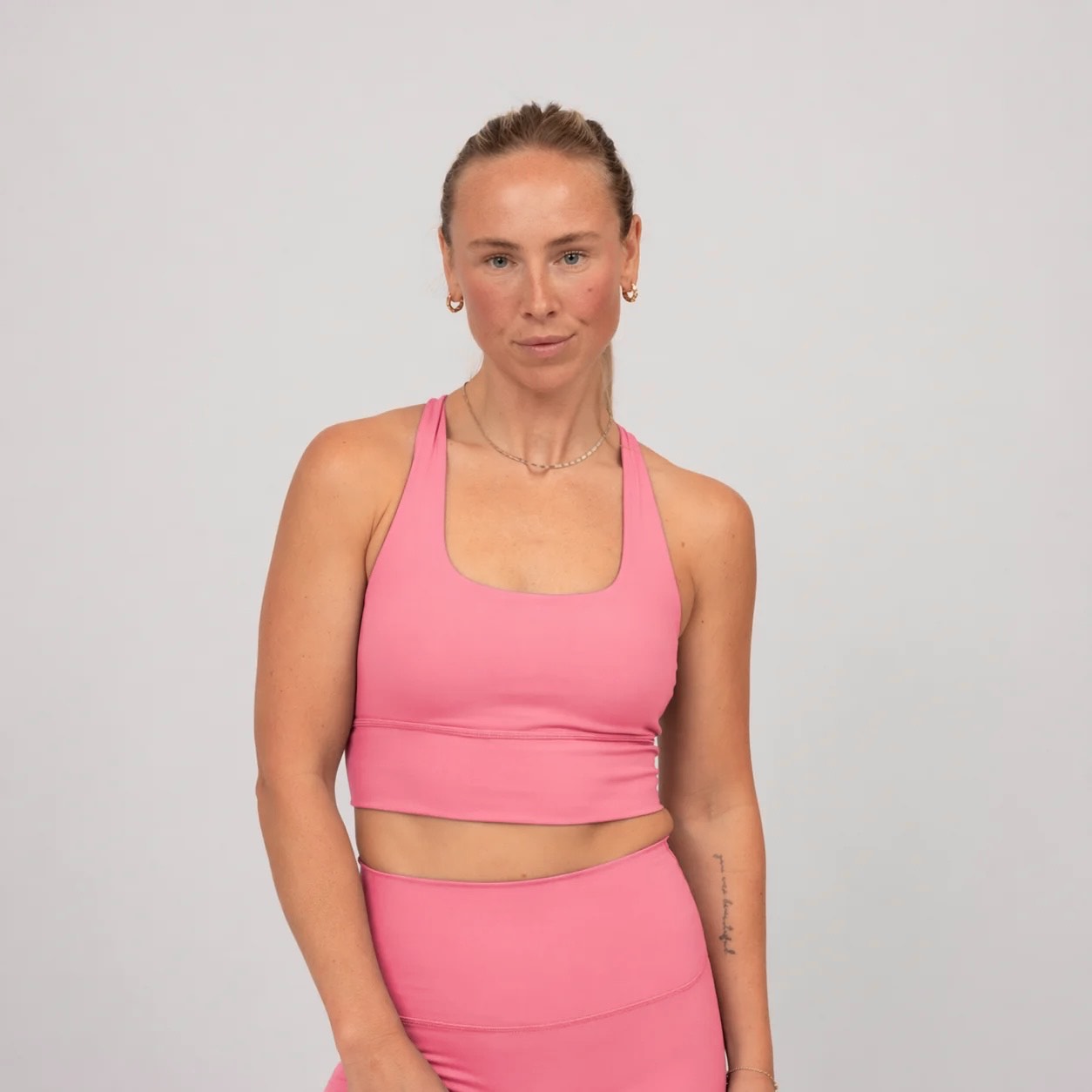 Woman wearing a pink Hybryd sports bra and leggings on a light gray background