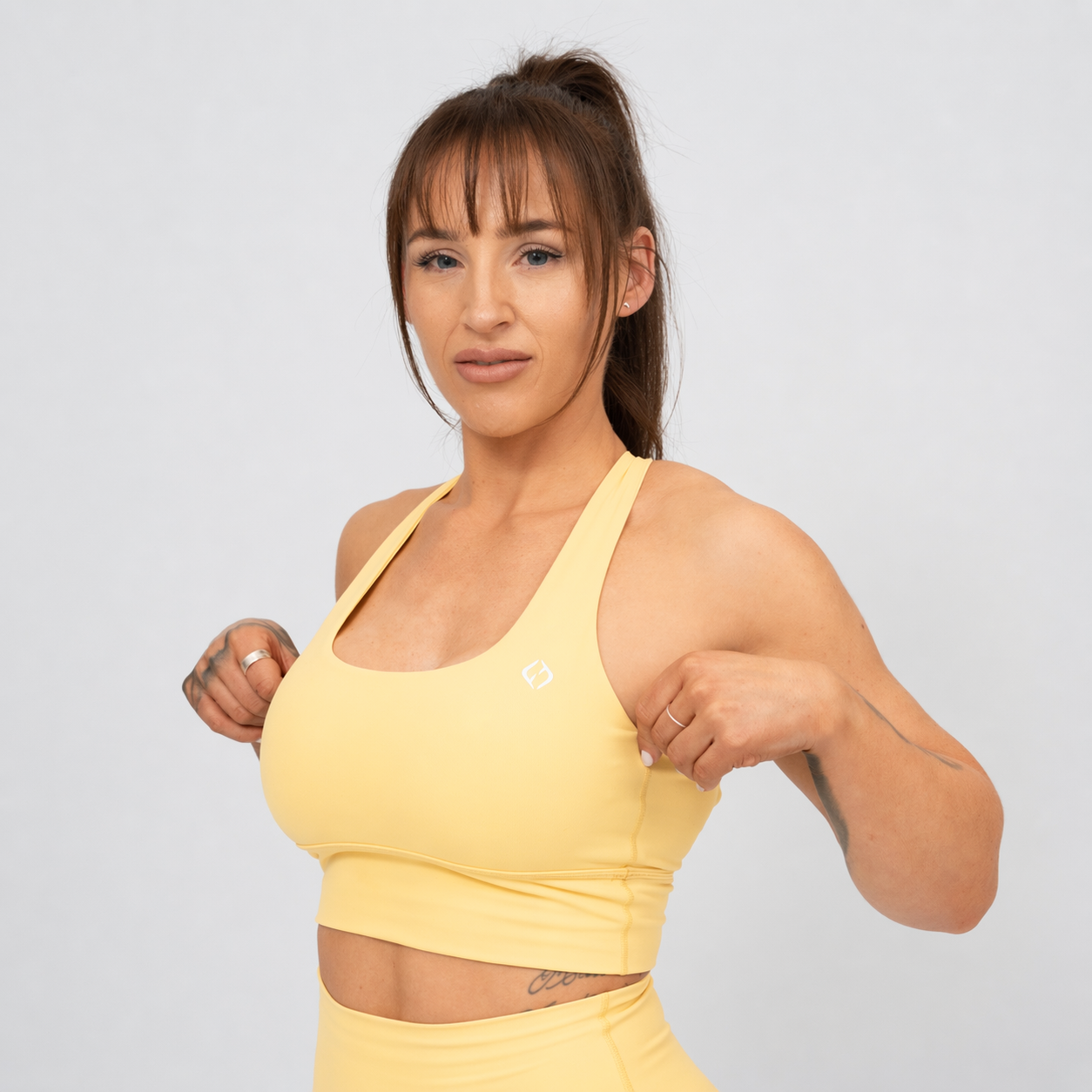 Woman wearing a yellow Hybryd sports bra and leggings on a light gray background