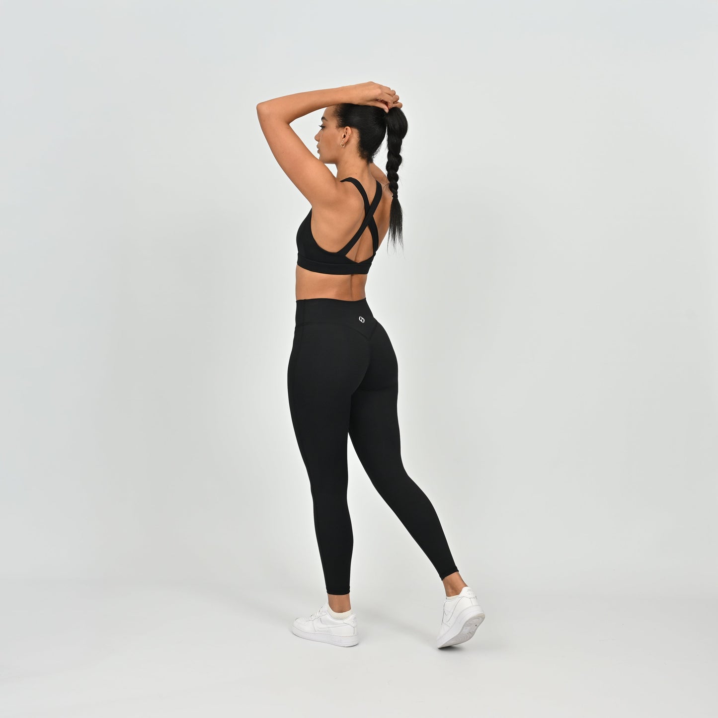 Woman wearing a black Hybryd sports bra and scrunch leggings on a light gray background