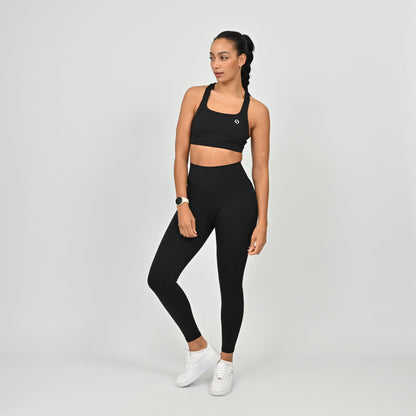 Woman wearing a black Hybryd sports bra and leggings set on a light gray background