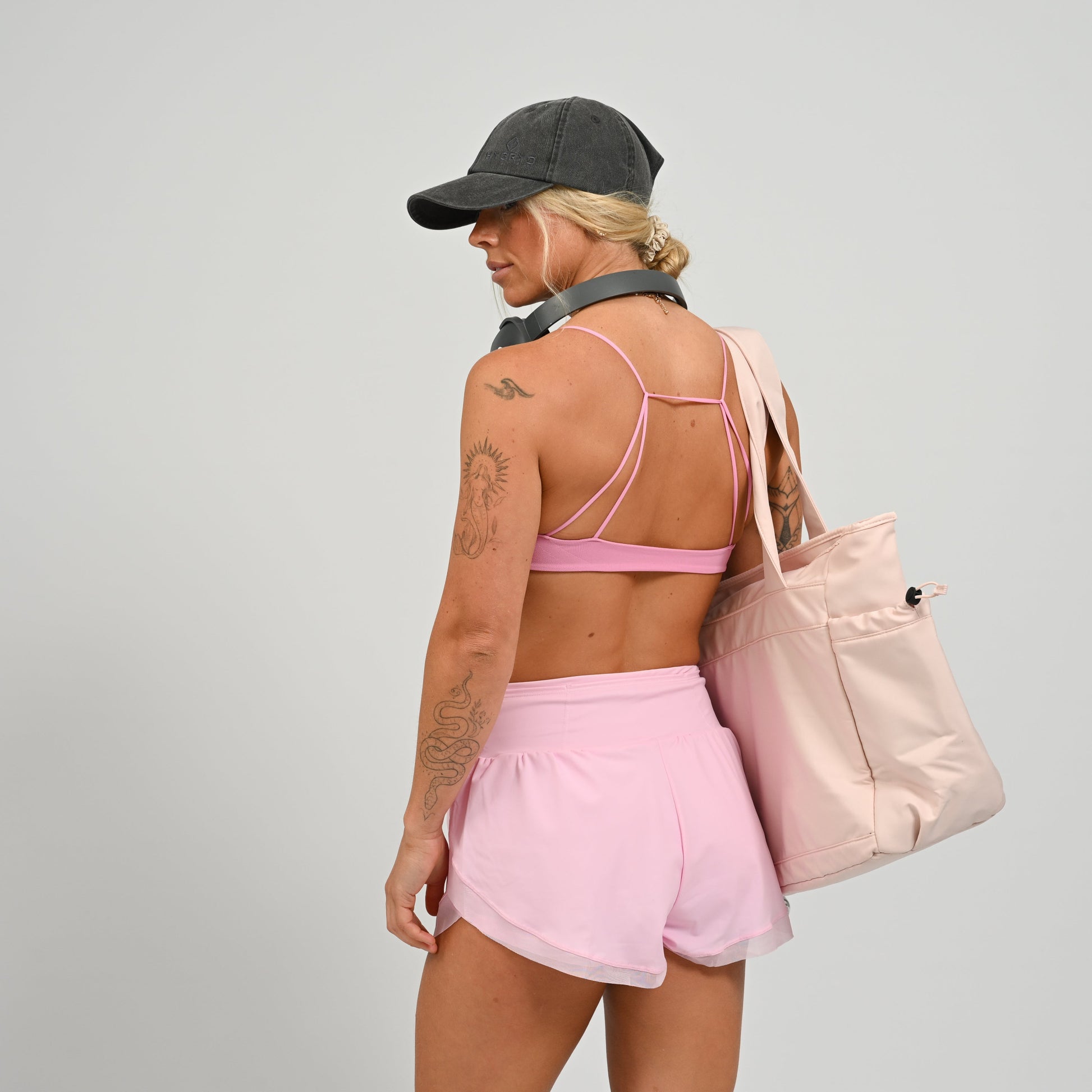 Hybryd athlete in pink athletic wear carrying a matching studio tote bag on a plain background