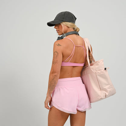 Hybryd athlete in pink athletic wear carrying a matching studio tote bag on a plain background