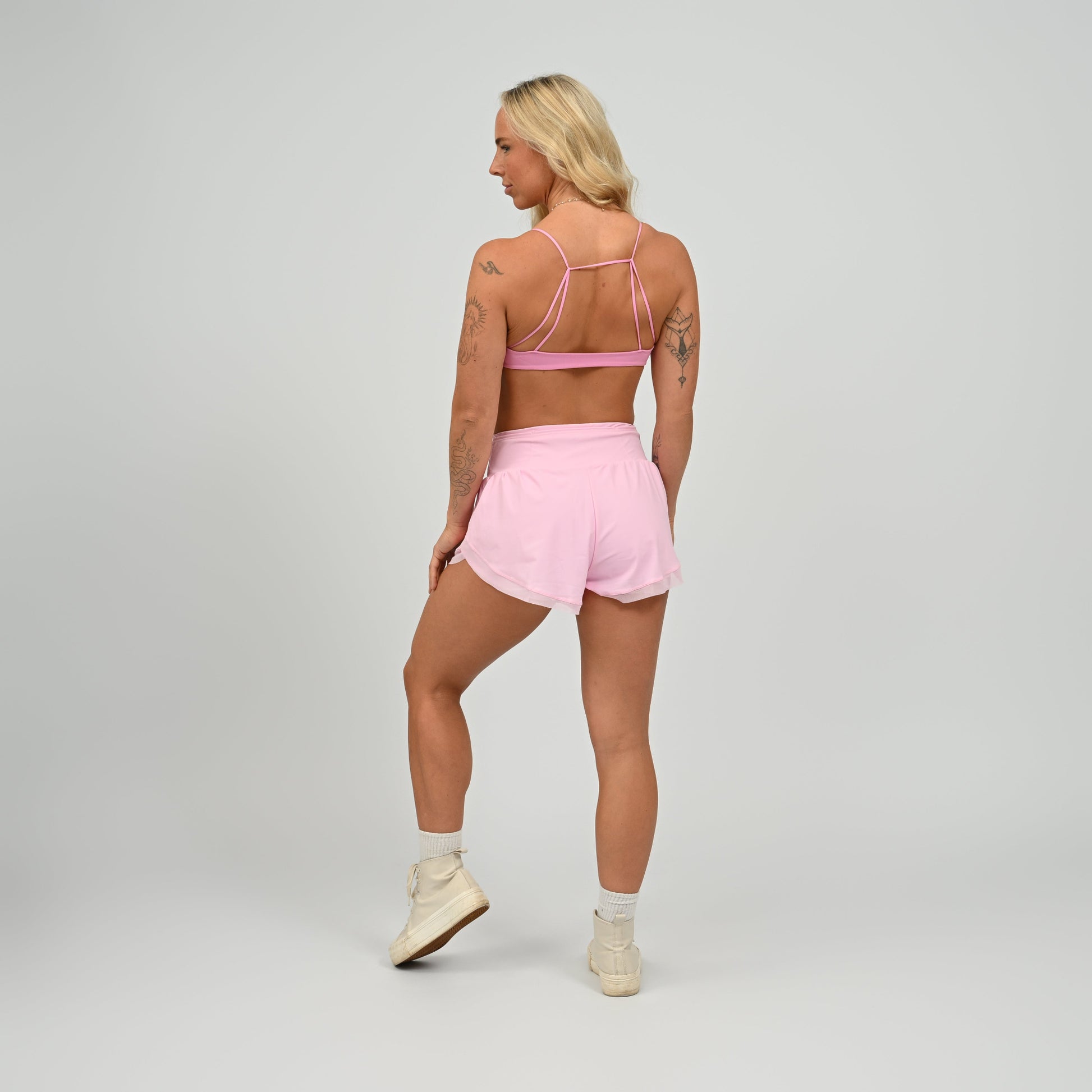 Hybryd athlete wearing a pink minimal sports bra and running shorts set on a gray background