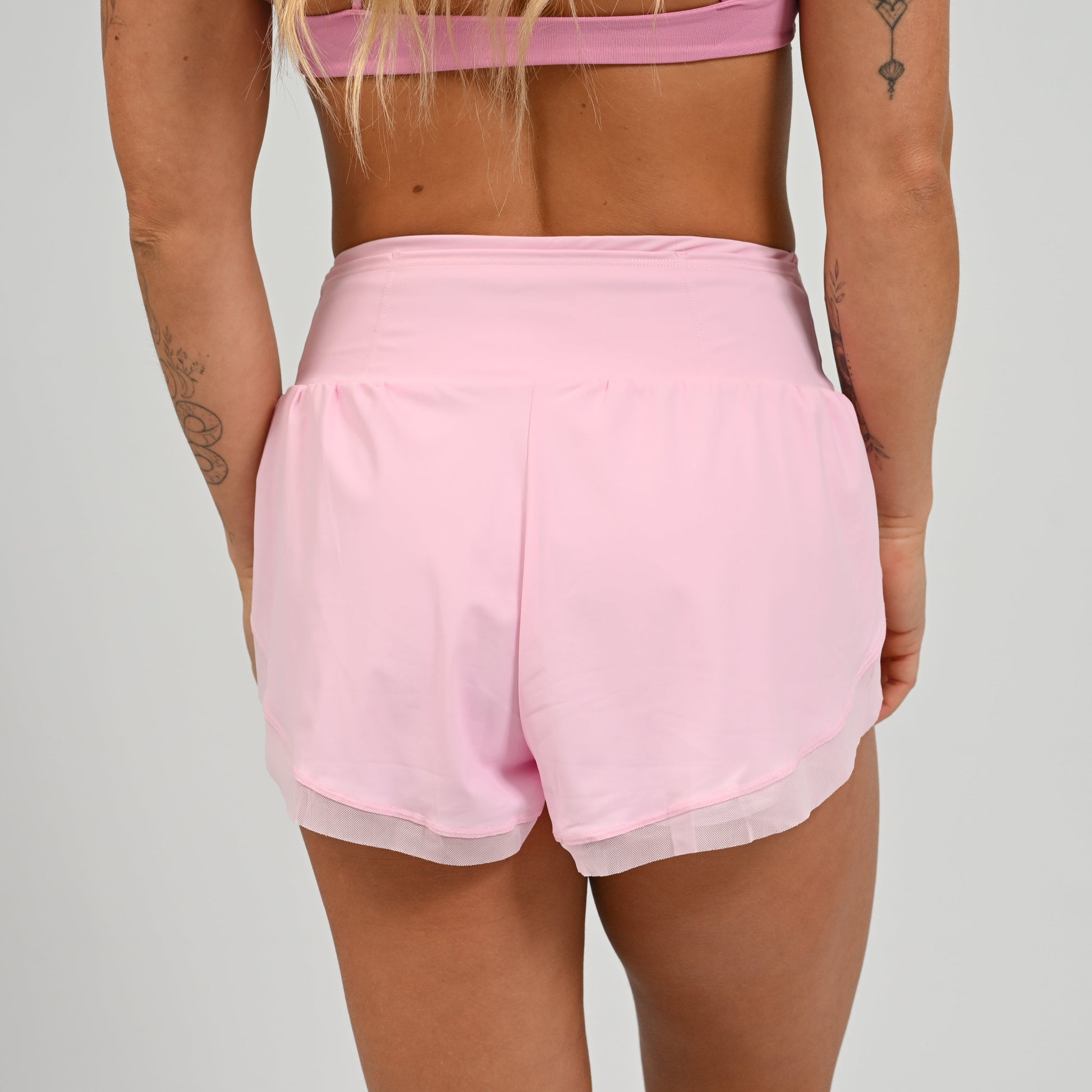 Athlete wearing pink running shorts and matching sports bra on a plain background