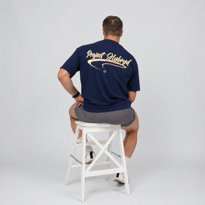 Men’s navy oversized gym T-shirt featuring a large cream Project Hybryd graphic across the back. He is sat on a stool with grey workout shorts. From clothing brand Hybryd