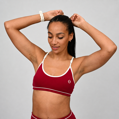 Female crossfit athlete wearing a red minimal sports bra with white adjustable straps against a gray background