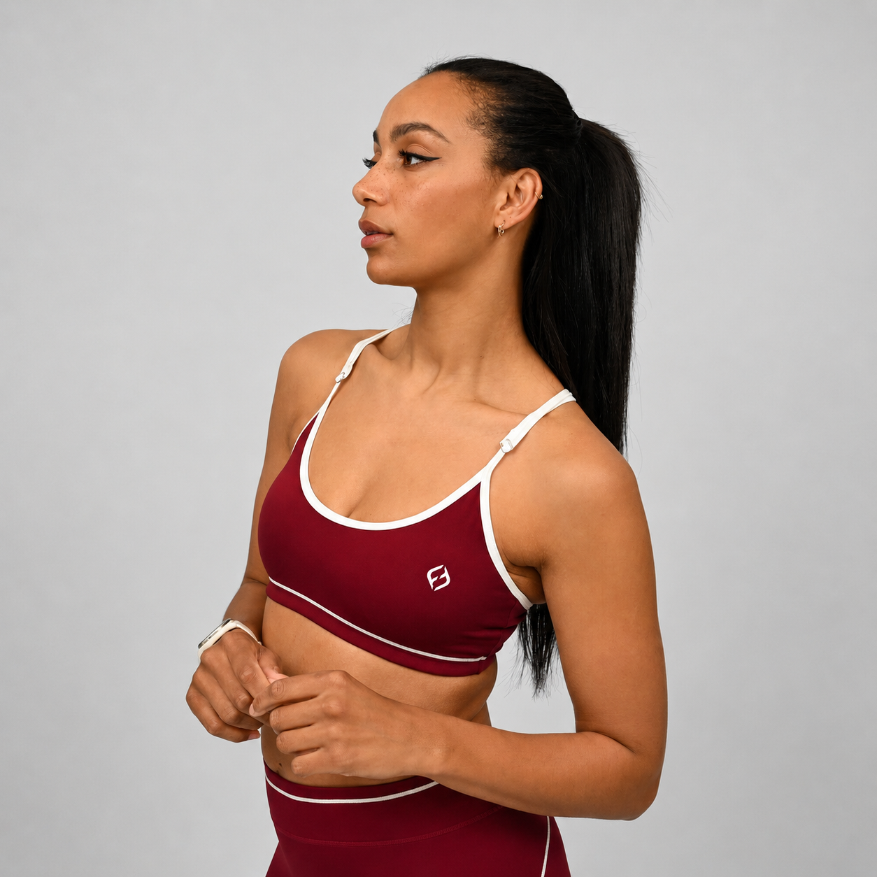 Hybryd athlete wearing a maroon sports bra with white piping detail and adjustable straps on a gray background