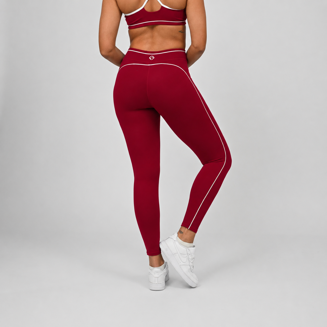 Hybryd athlete wearing red gym leggings with white piping and contouring with a minimal bra on a gray background