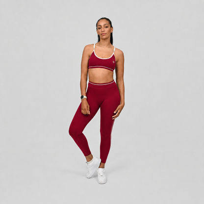 Pilates athlete wearing a red gym set with piped detail on a gray background