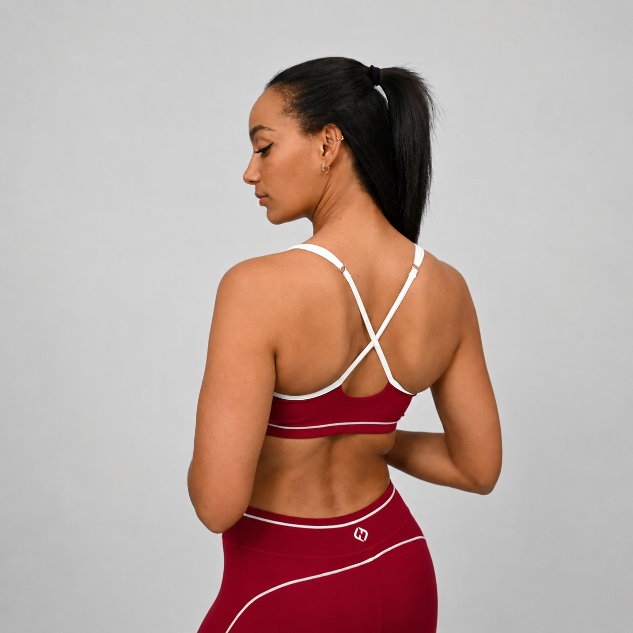 Crossfit athlete wearing a red Hybryd sports bra and leggings with piping detail and white straps on a gray background