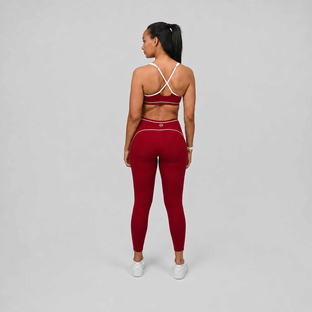 Athlete wearing a red Hybryd pilates sports bra and leggings set with white piping detail on a gray background