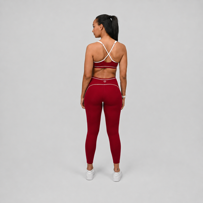 Athlete wearing a red Hybryd pilates sports bra and leggings set with white piping detail on a gray background