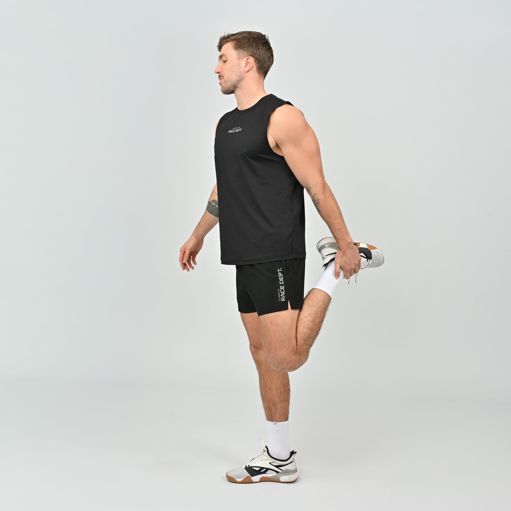Man wearing a black sleeveless running tank and shorts, stretching.