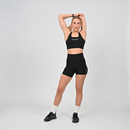 Woman wearing a black Hybryd sports bra and shorts with a white background