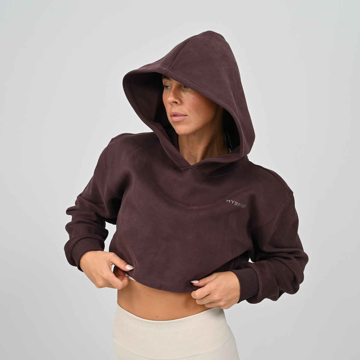 Front view of model wearing the aubergine Hybryd Barstow cropped hoodie with hood up   