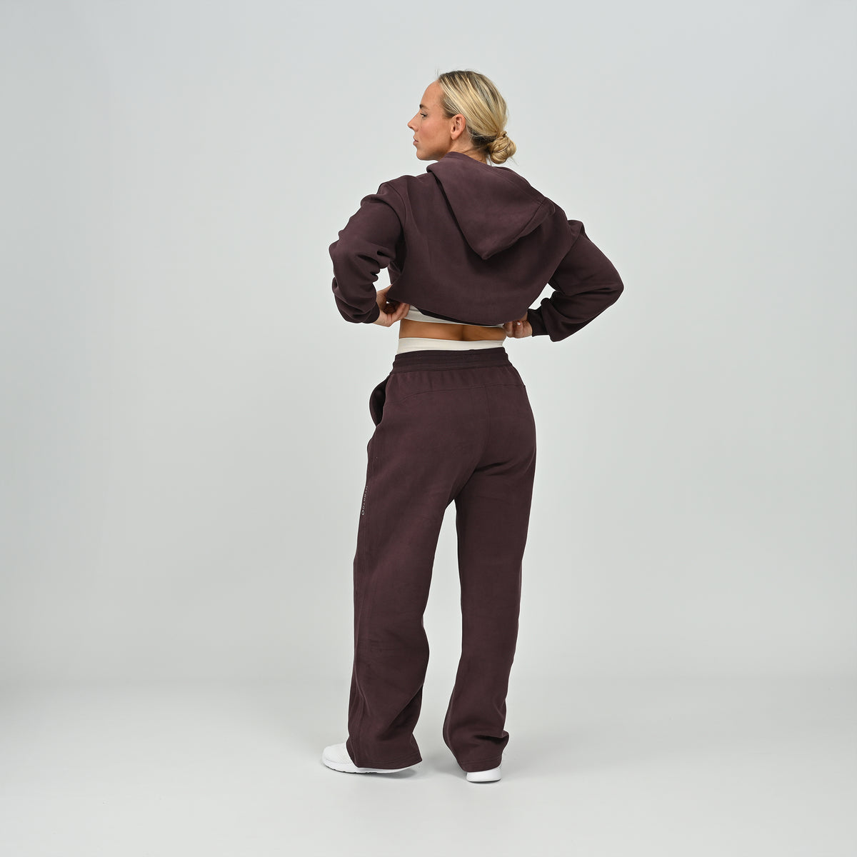 Full length back view of model posing in the aubergine Hybryd Barstow cropped hoodie and wide leg joggers set