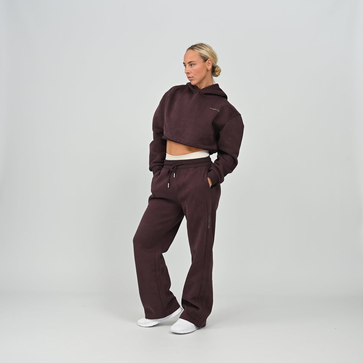 Studio shot of model wearing the aubergine Hybryd Barstow cropped hoodie and matching wide leg joggers set