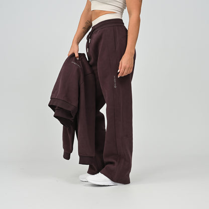 Model standing front view wearing the aubergine Hybryd Barstow wide leg joggers with cropped hoodie in hand