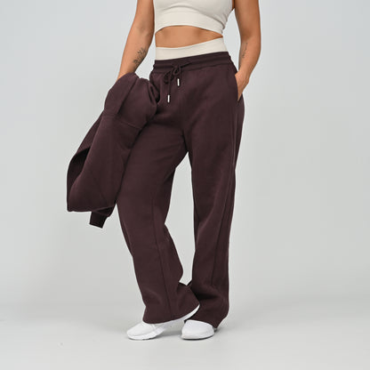 Front view of model wearing the aubergine Hybryd Barstow wide leg joggers with matching cropped hoodie over arm