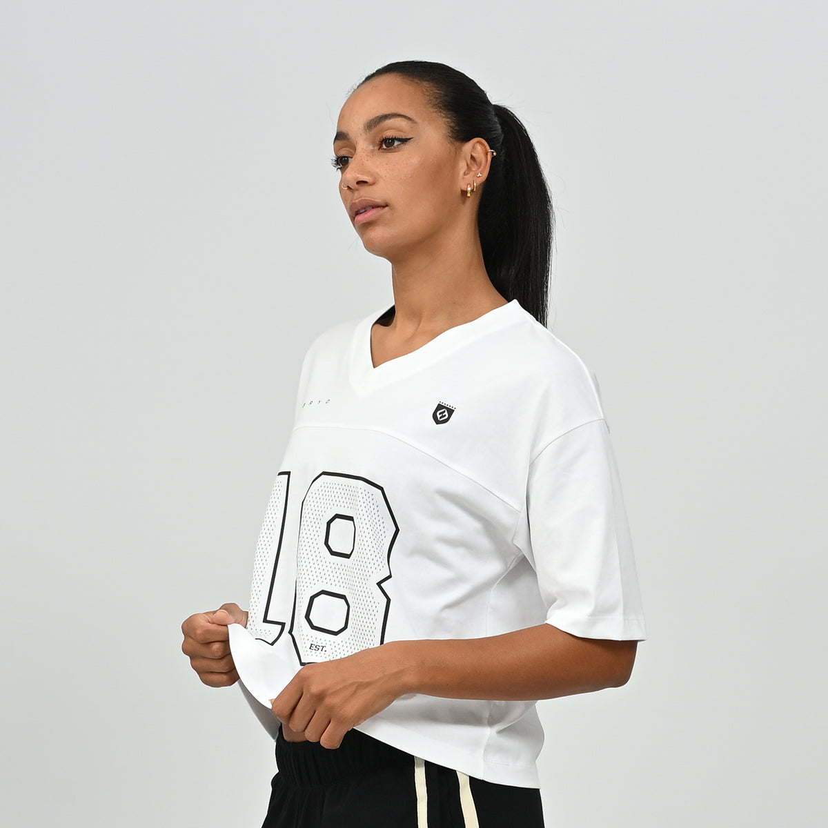 Mid-shot of a model wearing the white HAFT collegiate American football jersey tee by Hybryd holding the hem.