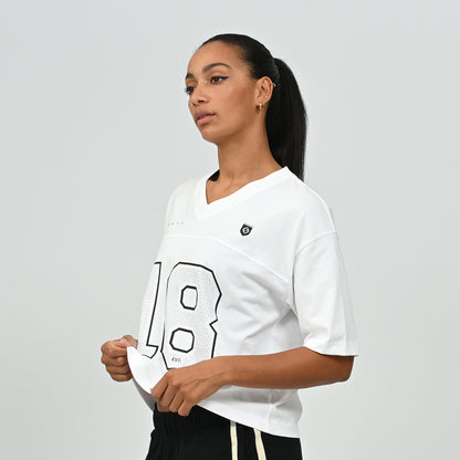 Mid-shot of a model wearing the white HAFT collegiate American football jersey tee by Hybryd holding the hem.