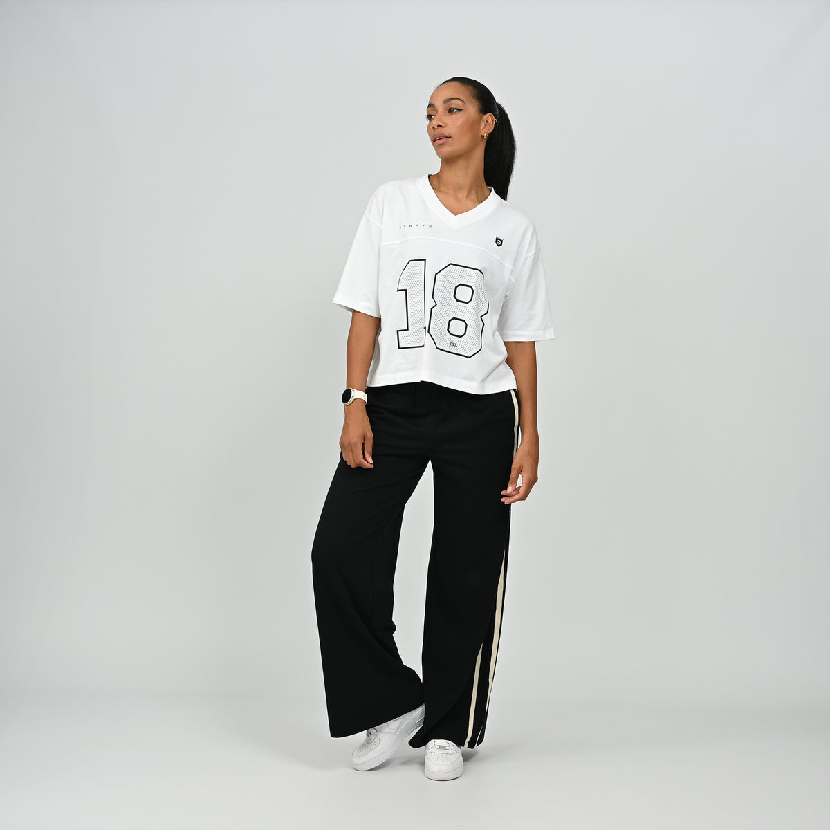 Front view of a model wearing the white HAFT collegiate style American football jersey t-shirt by Hybryd with black side-striped trousers.