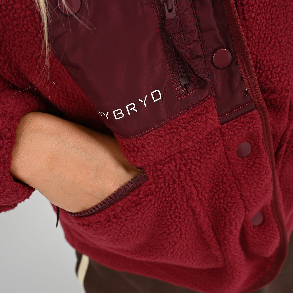 Close-up view of zipped pocket on women's wine burgundy Hybryd Huntsville teddy bear fleece jacket