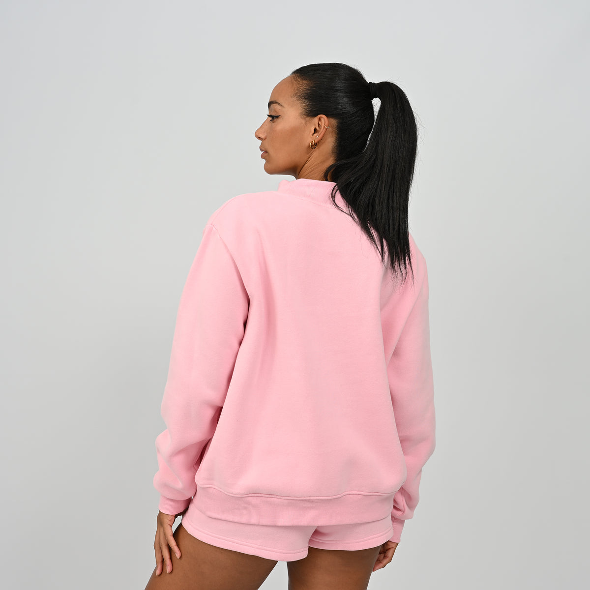 Back view of model wearing the pink Hybryd Scottsdale oversized crewneck sweatshirt and matching shorts set   
