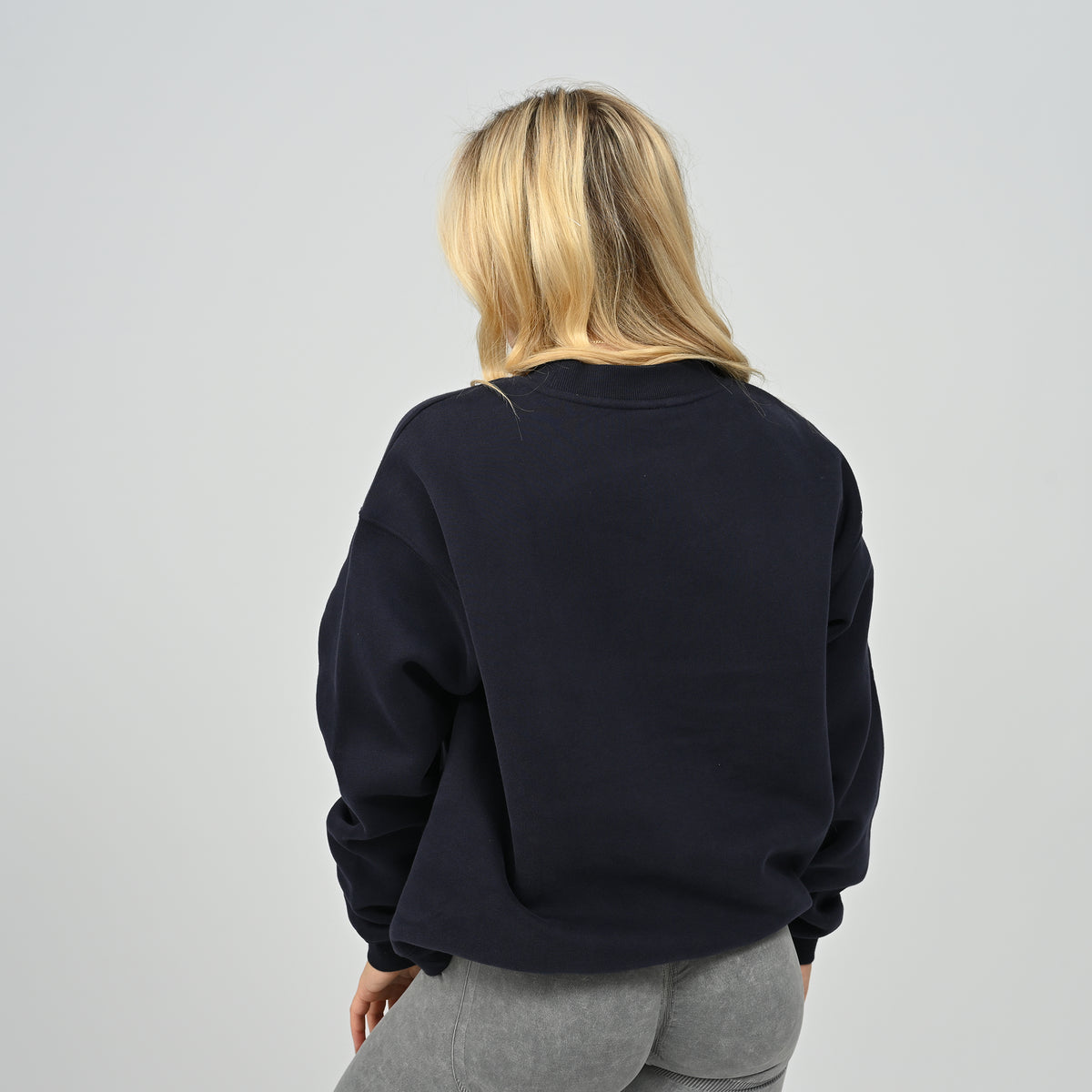 Rear view of female model wearing the Women's Hybryd Jasper fleece crew neck sweatshirt in navy with ribbed hem.