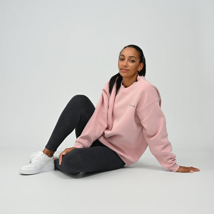 Seated lifestyle pose of female model wearing the Hybryd Women's Jasper crew neck sweatshirt in pink.