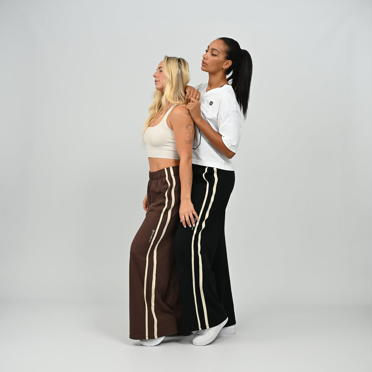 Model leaning on model in black and brown Hybryd Milford wide leg joggers   