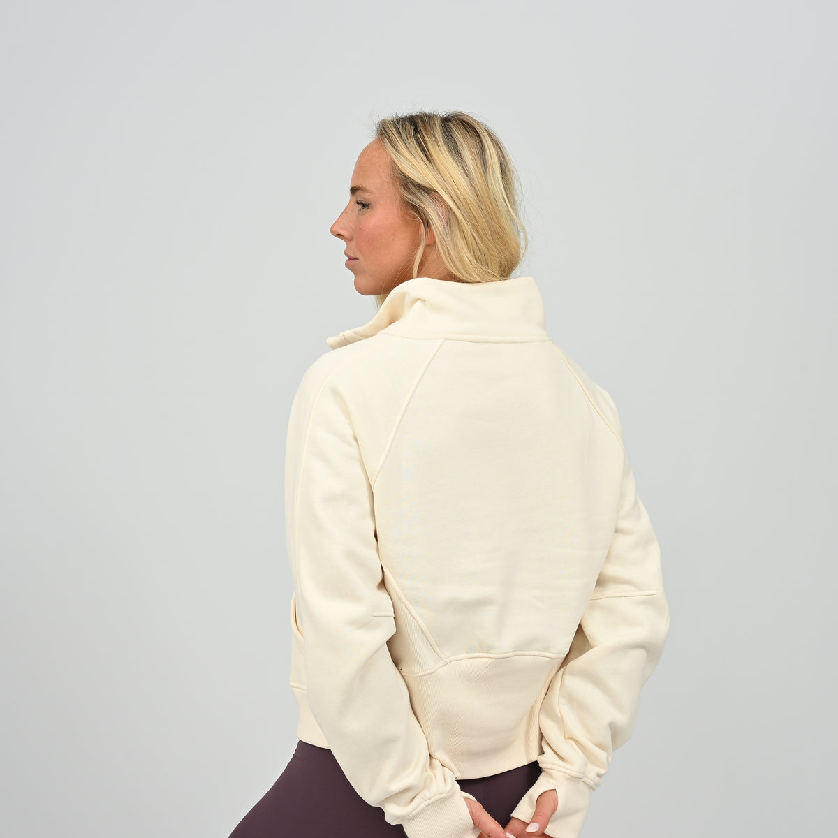 Back view of model wearing the cream Hybryd Monterey half zip sweatshirt showing paneled construction