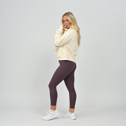 Full length view of model standing in the cream Hybryd Monterey half zip sweatshirt paired with leggings