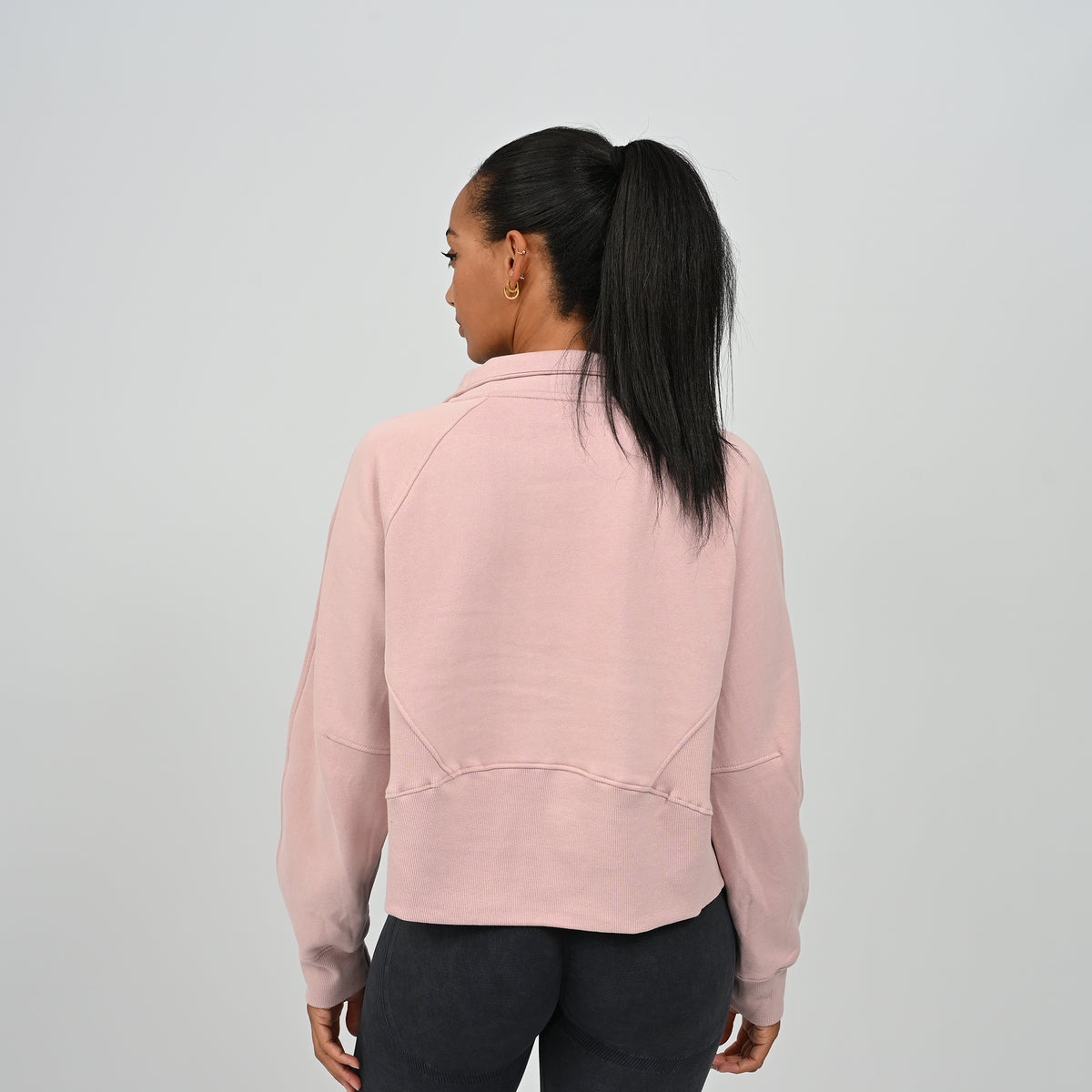 Back view of model wearing the dusty pink Hybryd Monterey half zip sweatshirt showing ribbed panel construction