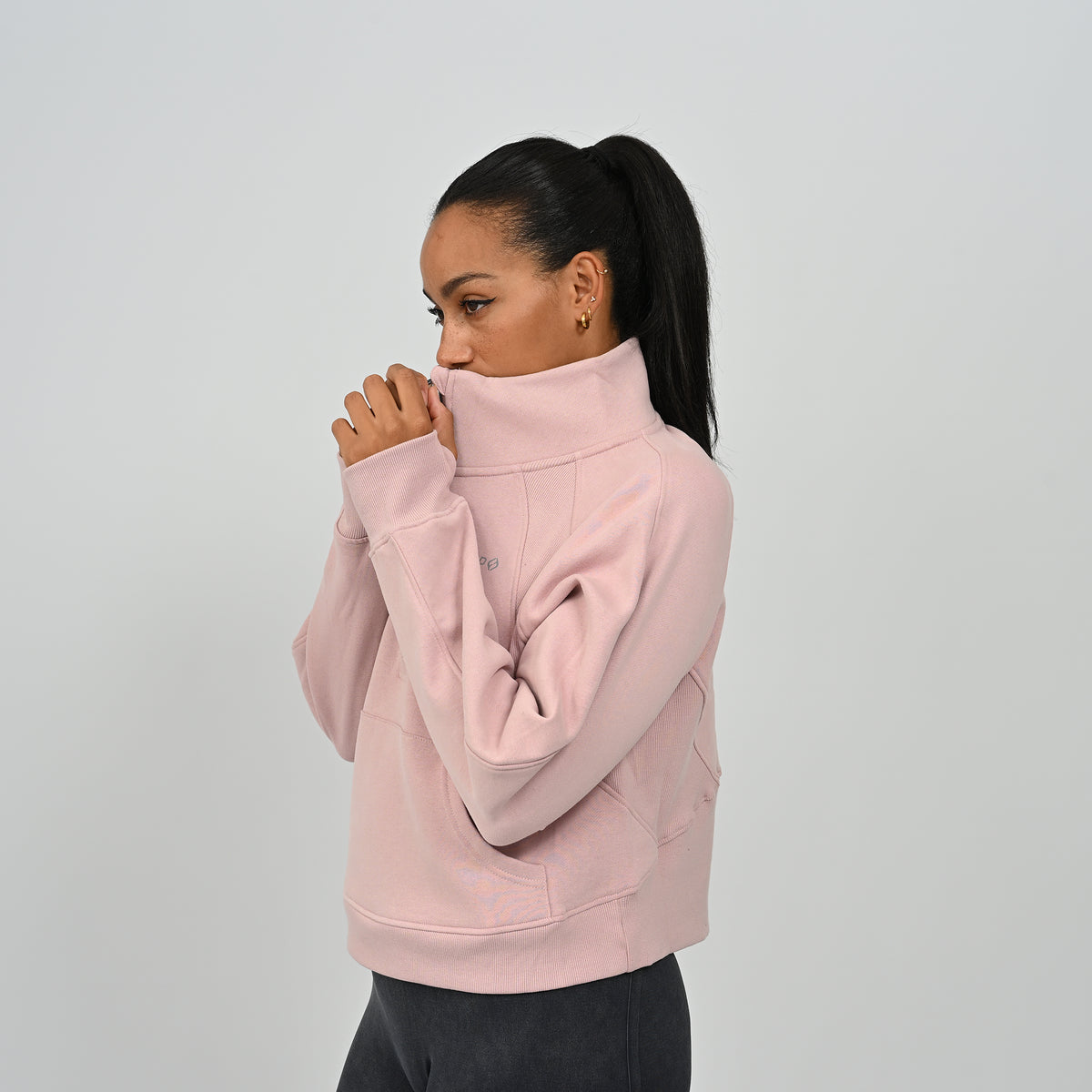 Close-up shot of model adjusting the zipped high collar on the dusty pink Hybryd Monterey half zip sweatshirt